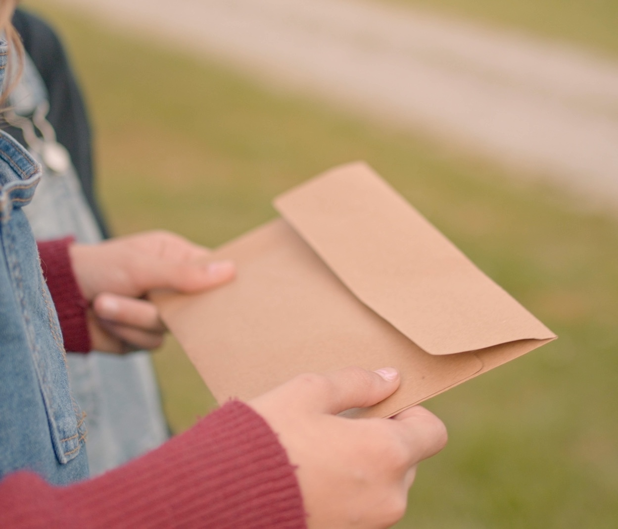 A child in a burgundy sweater and denim jacket holding a kraft paper envelope